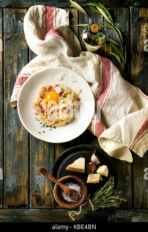 Tradizionale italiana la pasta alla carbonara con tuorlo d'uovo, pancetta, parmigiano, timo, servita nella piastra bianca sul tessile su un vecchio ceppo di legno bac Foto Stock