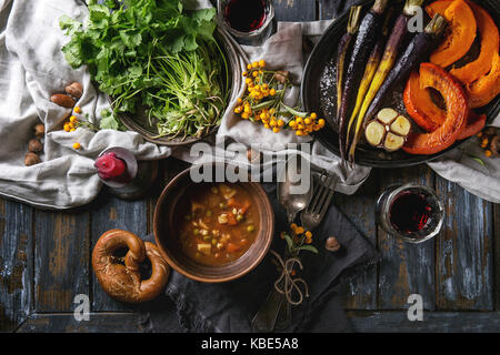 Holiday tabella di impostazione di decorazione con ciotole di zuppa calda, cottura zucca, carota, aglio, coriandolo fresco, salatini pane, vino rosso, bacche e candela Foto Stock