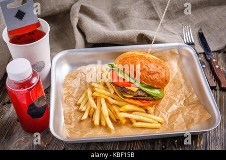 Grandi hamburger con tre fettine di manzo e verdure con dorate e croccanti patatine fritte e tostato toast croccanti su uno sfondo di legno. Foto Stock