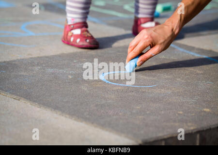 Piccola ragazza gamba e disegno di mom blue chalk sul parco giochi. Foto Stock