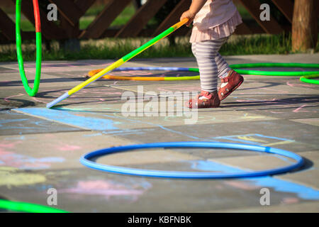 Piccola ragazza giocare hula hoops sul parco giochi graffiato con Chalk. Foto Stock