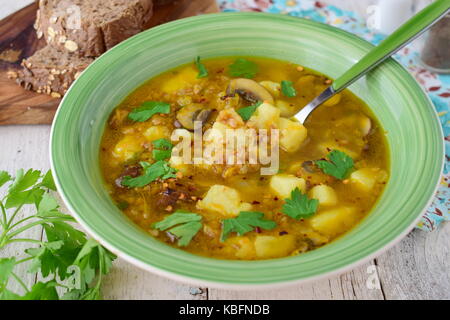 Una sana zuppa di grano saraceno, di fecola di patate, i funghi, la carota e la cipolla wit di olio di oliva in una ciotola verde su uno sfondo di legno. Foto Stock