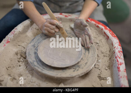 La sezione centrale del potter femmina piastra di stampaggio con lo strumento Mano nel laboratorio di ceramica Foto Stock