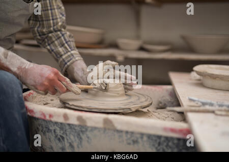La sezione centrale del potter maschio piastra di stampaggio con lo strumento Mano nel laboratorio di ceramica Foto Stock