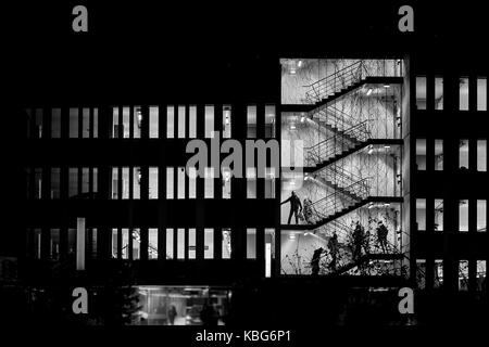 Immagine dell edificio del parcheggio di notte che mostra i contorni delle persone andando su e giù per i livelli. aprendo le porte alla ricerca per le loro auto. Foto Stock