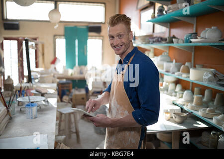 Ritratto di potter maschio utilizzando tavoletta digitale nel laboratorio di ceramica Foto Stock
