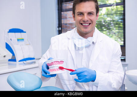 Ritratto di dentista spazzolatura stampo dentale mentre è seduto alla clinica Foto Stock