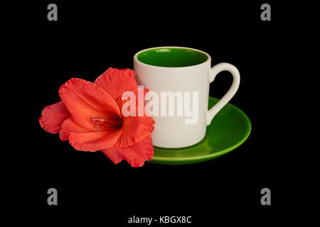 Una piccola tazza bianca con piattino e un intenso gladioli flower giacente su di esso Foto Stock