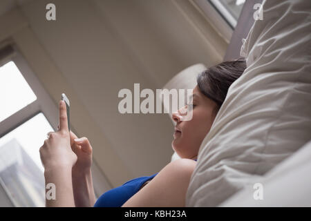 Donna che utilizza telefono mentre è sdraiato sul letto di casa Foto Stock
