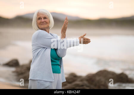 Felice senior donna facendo esercizio di stretching sulla spiaggia Foto Stock