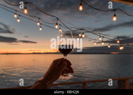 Tenendo alto il vino rosso sotto il ponte pensile luci al tramonto sul mare. Foto Stock