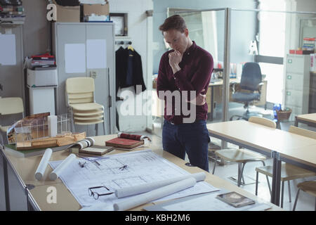 Architetto pensieroso guardando blueprint in studio Foto Stock