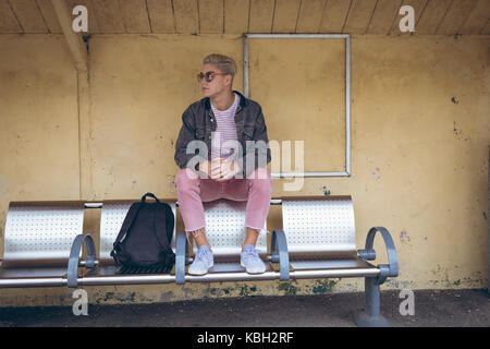 Riflessivo uomo seduto sulla panchina alla stazione ferroviaria Foto Stock