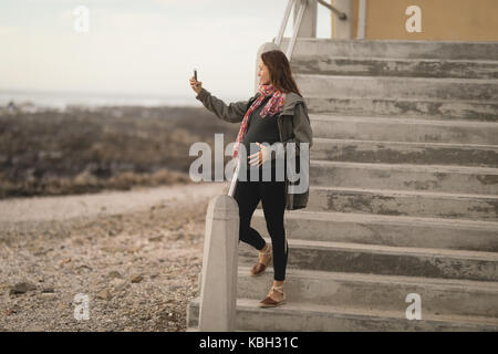 Donna incinta prendendo un selfie vicino alla spiaggia Foto Stock