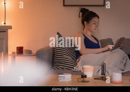 Giovane donna con tavoletta digitale sul divano di casa Foto Stock