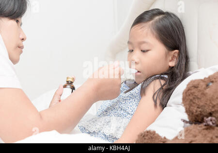 Madre asiatica dando sua figlia di sciroppo a causa dell'influenza in camera da letto, bambino malato e health care concept Foto Stock
