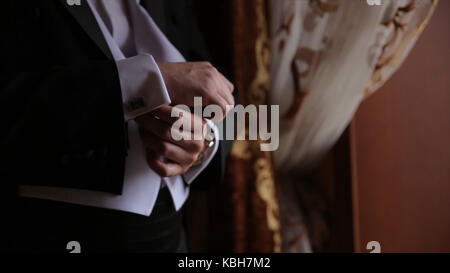 Lo sposo è tenendo le mani sul tirante, wedding suit. close up di un uomo a mano come indossa una camicia bianca e cufflink. business man di fissaggio tirante nero su bianco shirt. groom sul giorno di nozze fascetta di fissaggio, effetto vintage. primo piano di un uomo in abito nero la correzione di un manicotto di usura per lo sposo cufflink close up shot con vista mare. wedding Foto Stock