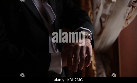 Lo sposo è tenendo le mani sul tirante, wedding suit. close up di un uomo a mano come indossa una camicia bianca e cufflink. business man di fissaggio tirante nero su bianco shirt. groom sul giorno di nozze fascetta di fissaggio, effetto vintage. primo piano di un uomo in abito nero la correzione di un manicotto di usura per lo sposo cufflink close up shot con vista mare. wedding Foto Stock