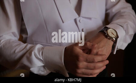 Lo sposo è tenendo le mani sul tirante, wedding suit. close up di un uomo a mano come indossa una camicia bianca e cufflink. business man di fissaggio tirante nero su bianco shirt. groom sul giorno di nozze fascetta di fissaggio, effetto vintage. primo piano di un uomo in abito nero la correzione di un manicotto di usura per lo sposo cufflink close up shot con vista mare. wedding Foto Stock