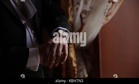 Lo sposo è tenendo le mani sul tirante, wedding suit. close up di un uomo a mano come indossa una camicia bianca e cufflink. business man di fissaggio tirante nero su bianco shirt. groom sul giorno di nozze fascetta di fissaggio, effetto vintage. primo piano di un uomo in abito nero la correzione di un manicotto di usura per lo sposo cufflink close up shot con vista mare. wedding Foto Stock