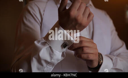 Lo sposo è tenendo le mani sul tirante, wedding suit. close up di un uomo a mano come indossa una camicia bianca e cufflink. business man di fissaggio tirante nero su bianco shirt. groom sul giorno di nozze fascetta di fissaggio, effetto vintage. primo piano di un uomo in abito nero la correzione di un manicotto di usura per lo sposo cufflink close up shot con vista mare. wedding Foto Stock