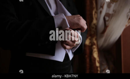 Lo sposo è tenendo le mani sul tirante, wedding suit. close up di un uomo a mano come indossa una camicia bianca e cufflink. business man di fissaggio tirante nero su bianco shirt. groom sul giorno di nozze fascetta di fissaggio, effetto vintage. primo piano di un uomo in abito nero la correzione di un manicotto di usura per lo sposo cufflink close up shot con vista mare. wedding Foto Stock