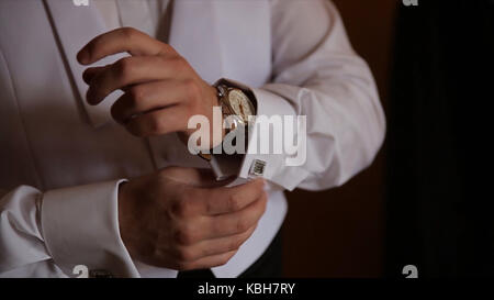 Lo sposo è tenendo le mani sul tirante, wedding suit. close up di un uomo a mano come indossa una camicia bianca e cufflink. business man di fissaggio tirante nero su bianco shirt. groom sul giorno di nozze fascetta di fissaggio, effetto vintage. primo piano di un uomo in abito nero la correzione di un manicotto di usura per lo sposo cufflink close up shot con vista mare. wedding Foto Stock