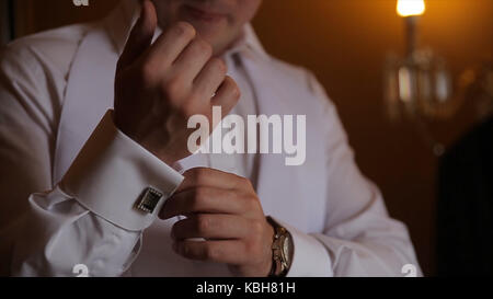 Lo sposo è tenendo le mani sul tirante, wedding suit. close up di un uomo a mano come indossa una camicia bianca e cufflink. business man di fissaggio tirante nero su bianco shirt. groom sul giorno di nozze fascetta di fissaggio, effetto vintage. primo piano di un uomo in abito nero la correzione di un manicotto di usura per lo sposo cufflink close up shot con vista mare. wedding Foto Stock