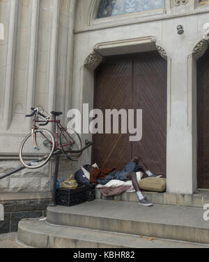 Senzatetto uomo con la sua bicicletta dorme all'ingresso di una chiesa sulla settima avenue a Park Slope di Brooklyn, NY. Foto Stock