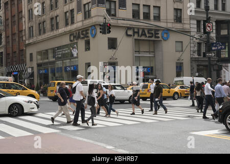 Pedoni cross 34th street sulla quinta avenue con un onnipresente chase bank branch in background in midtown Manhattan. Foto Stock