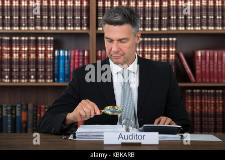 Maschio maturo auditor scrutare i documenti finanziari a tavola in office Foto Stock