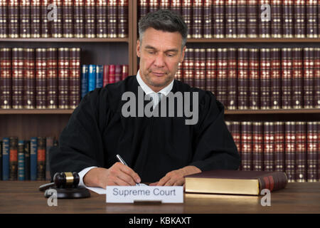 Maschio maturo giudicare la scrittura su carta a tavola nelle aule di tribunale Foto Stock