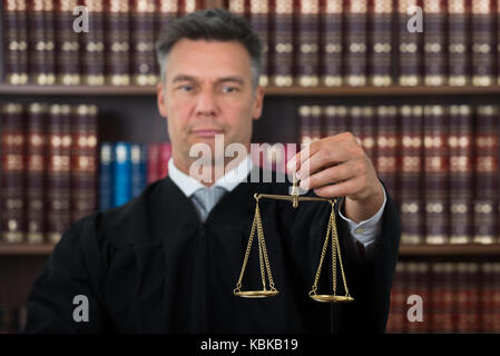 Maschio maturo giudicare tenendo la giustizia scala contro scaffale in aula Foto Stock