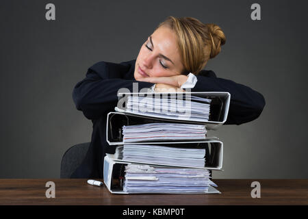 Stanco imprenditrice dormire su leganti impilati su sfondo nero Foto Stock