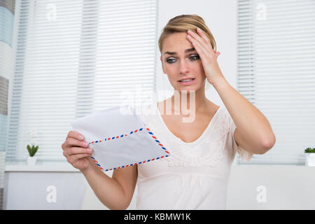 Scioccato giovane donna lettura la lettera mentre si tocca la testa a casa Foto Stock