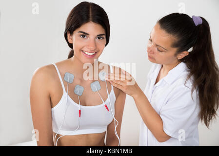 Terapista posizionare gli elettrodi su buon torace della donna Foto Stock