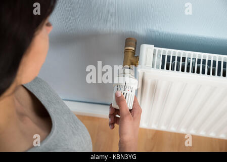 Elevato angolo di visione della donna ruotando il termostato del radiatore a casa Foto Stock
