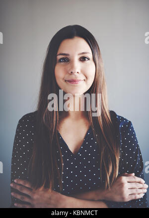 Ritratto di un attraente giovane imprenditrice sorridere mentre in piedi da solo in un ufficio con le braccia incrociate Foto Stock