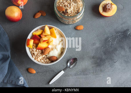 In casa i fiocchi d'avena muesli con yogurt e pesche in un recipiente per una sana prima colazione. a base di cereali e frutta tazza colazione con yogurt. Foto Stock