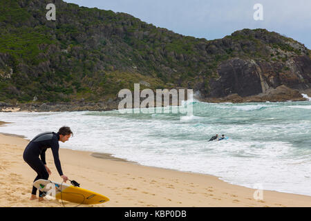 L'uomo con la sua tavola da surf sulla spiaggia a forma di boomerang andando per la mattina presto surf,Mid north coast, Nuovo Galles del Sud, Australia Foto Stock