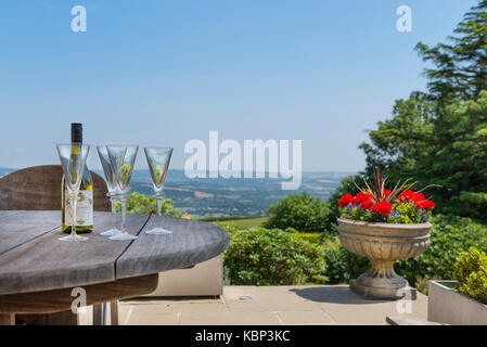 Bottiglia di vino e bicchieri di sedersi su un giardino in legno tabella contro una stupenda vista Dartmoor nel devon su una soleggiata giornata estiva. costa di frutti di mare Foto Stock