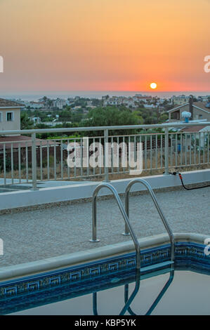 La piscina e il tramonto sul villaggio e sul mare orizzonte Foto Stock