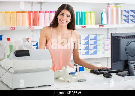 Ritratto di giovane sorridente commessa permanente al registratore di cassa nel supermercato Foto Stock