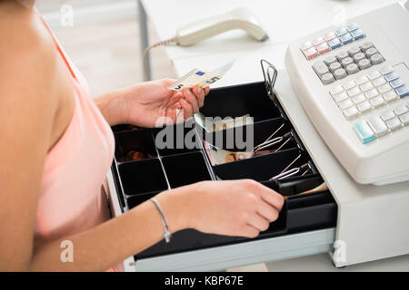 Angolo di alta vista del cassiere femminile alla ricerca di cambiamento di registro di cassa cassetto al supermercato Foto Stock