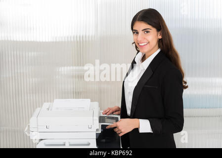 Giovane imprenditrice utilizzando macchina fotocopiatrice in ufficio Foto Stock