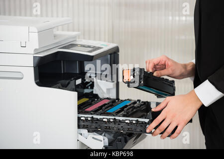 Sezione mediana del giovane imprenditore che fissa la cartuccia nella stampante in ufficio Foto Stock