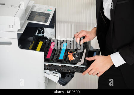 Sezione mediana del giovane imprenditore che fissa la cartuccia nella stampante in ufficio Foto Stock