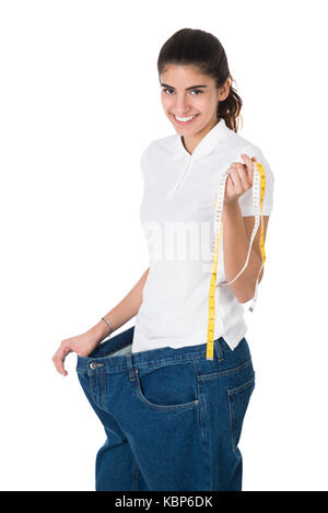 Ritratto di sorridente giovane donna con nastro di misurazione che mostra i suoi vecchi jeans su sfondo bianco Foto Stock
