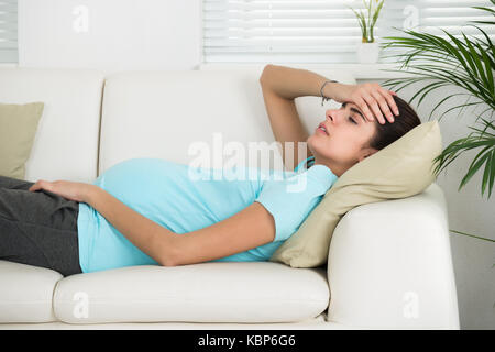 Vista laterale della giovane donna in stato di gravidanza che soffrono di mal di testa a casa Foto Stock