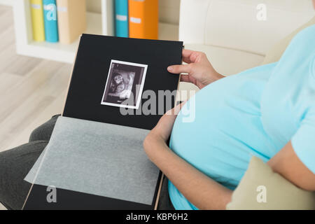 Sezione mediana della donna incinta con scansione a ultrasuoni seduti sul divano di casa Foto Stock